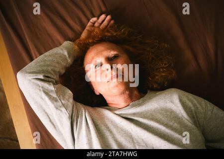 Vue à grand angle de la femme senior réfléchie couchée sur le lit à la maison Banque D'Images