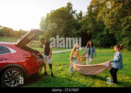 Les sœurs s'entraident tout en posant une couverture sur l'herbe au parc Banque D'Images