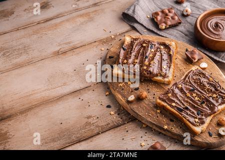 Planche de pain avec pâte de chocolat et bonbons de fête saupoudrer et noisettes sur fond de bois. Nourriture populaire de dessicer. Vue de dessus. Banque D'Images