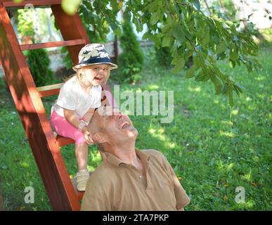 Petite fille léchant sucette sucette et grand-père jouant et riant sur les escaliers en bois Banque D'Images