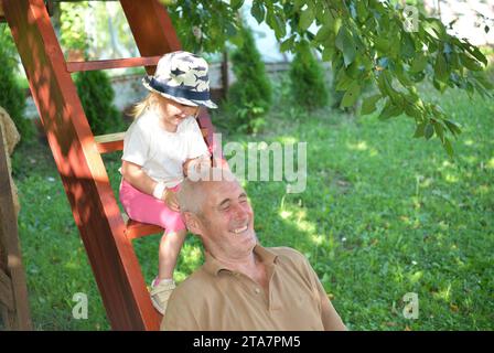 Petite fille léchant sucette sucette et grand-père jouant et riant sur les escaliers en bois Banque D'Images