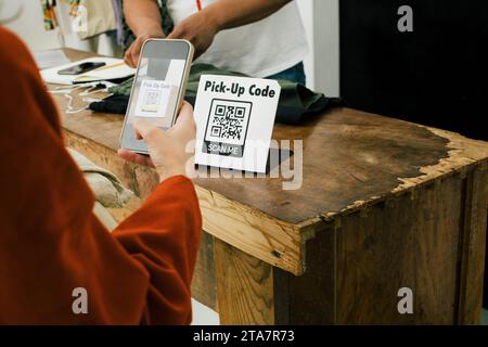 Client féminin scannant le code-barres via le téléphone intelligent tout en payant au magasin de vêtements Banque D'Images