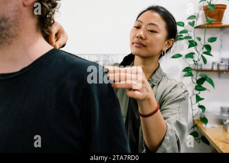 Femme tailleur mesurant l'épaule du client masculin à l'atelier Banque D'Images