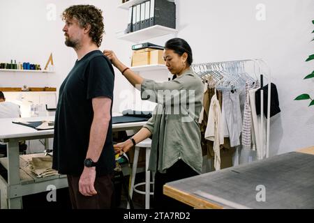 Femme tailleur prenant des mesures de client masculin à l'atelier Banque D'Images