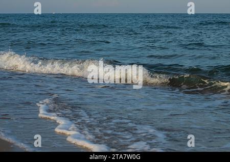 Une grande et forte onde de tempête de couleur turquoise avec des éclaboussures de mousse blanche coule et se brise sur le rivage. Banque D'Images