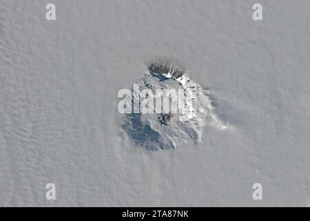 25 novembre 2023 - Antarctique - le cratère sommital du mont Erebus, le volcan actif le plus méridional du monde, est apparu au-dessus des nuages à la fin du printemps 2023. L'OLI-2 sur Landsat 9 a capturé cette vue du stratovolcan le 25 novembre. Le mont Erebus est l'un des volcans formant l'île Ross au large de la côte ouest de l'Antarctique. À 3 794 mètres (12 450 pieds) au-dessus du niveau de la mer, il surplombe la gare de McMurdo, située à seulement 35 kilomètres (22 miles). Ces volcans se produisent dans une zone de rift où l'extension a fait amincir la croûte et a permis au magma de migrer vers le haut à travers des failles vers le sur Banque D'Images