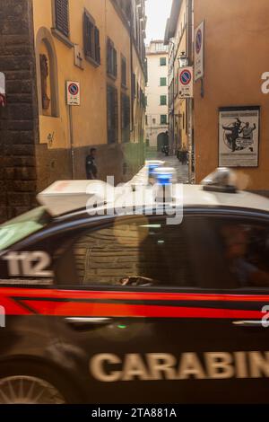 Une voiture de carabineros passe à toute vitesse devant un jeune homme appuyé sur un mur. Une affiche d'une école d'arts martiaux est vue sur un mur, Florence, Italie Banque D'Images