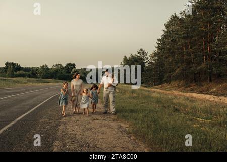 Maman, papa et filles marchent le long d'une route rurale le long de la forêt. Une famille heureuse Banque D'Images