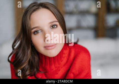 Gros plan d'une femme avec un sourire sincère, portant un pull rouge confortable, capturant un moment de bonheur authentique Banque D'Images