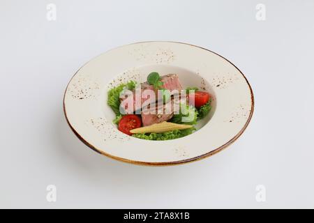 Steak de thon, laitue et légumes dans une belle assiette sur fond blanc, restaurant servant. Banque D'Images