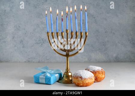 Menorah avec des bougies allumées, beignets savoureux et cadeau pour la célébration Hanukkah sur fond grunge Banque D'Images