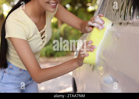 Femme lavant la voiture avec une éponge à l'extérieur, gros plan Banque D'Images
