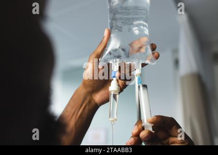 Gros plan d'un médecin afro-américain appliquant le goutte-à-goutte en chambre d'hôpital Banque D'Images