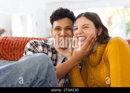 Portrait d'heureux couple diversifié assis sur le canapé et faire des visages drôles à la maison, espace de copie. Expression, loisirs, amour, unité, gesticulation, Banque D'Images