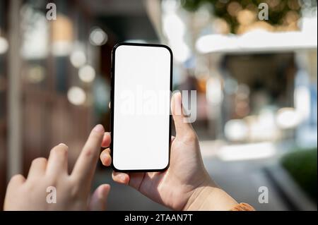 Image rapprochée d'une maquette de smartphone à écran blanc dans la main d'une femme avec un arrière-plan flou de magasins de détail dans la rue. services bancaires mobiles, à l'aide de ma Banque D'Images