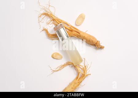 Vue de dessus de la bouteille vide affichée avec des racines fraîches de ginseng sur fond blanc. Le ginseng est un ingrédient largement utilisé dans les cosmétiques avec de nombreux avantages f Banque D'Images