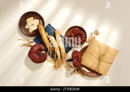 Scène pour la publicité de la médecine traditionnelle chinoise avec des herbes séchées décorées sur fond blanc. Racine de ginseng frais, champignons lingzhi et médicaments Banque D'Images