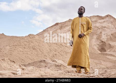 Vue grand angle d'un jeune homme noir portant un caftan traditionnel dans un paysage désertique, espace copie Banque D'Images