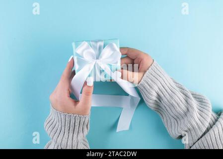 Première personne vue de dessus photo de mains féminines tenant la boîte cadeau bleue avec ruban blanc. Un décor bleu pastel accueille vos mots. mes mains bercent un passé Banque D'Images