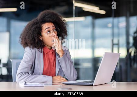 Ennuyeux travail quotidien à l'intérieur du bureau, femme d'affaires bâillant, travaillant sur le lieu de travail avec ordinateur portable, femme fatiguée travaillant tard avec ordinateur portable et documents, comptable financier. Banque D'Images