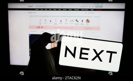 Personne tenant un téléphone portable avec le logo de la société britannique de vente au détail de vêtements Next plc devant la page Web de l'entreprise. Concentrez-vous sur l'affichage du téléphone. Banque D'Images