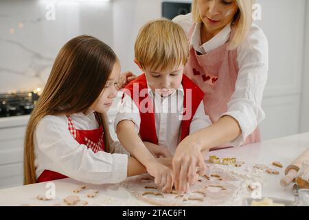 Les enfants et leur mère découpaient des biscuits de la pâte. Une petite fille et un garçon font des biscuits de Noël dans la cuisine. Banque D'Images