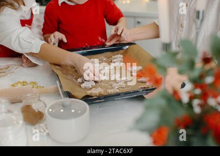 Une mère avec sa fille et son fils prépare des biscuits de Noël, les enfants mettent des biscuits sur une plaque de cuisson. Gros plan. Banque D'Images