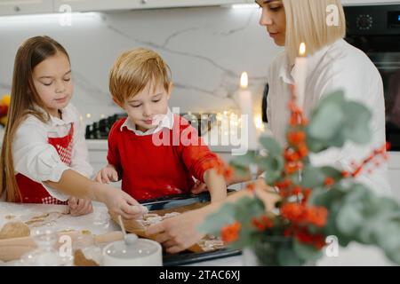 Une mère avec sa fille et son fils prépare des biscuits de Noël, les enfants mettent des biscuits sur une plaque de cuisson. Banque D'Images