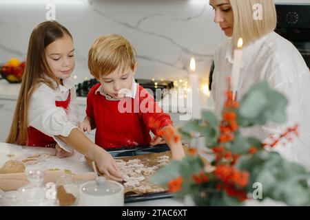 Une mère avec sa fille et son fils prépare des biscuits de Noël, les enfants mettent des biscuits sur une plaque de cuisson. Banque D'Images