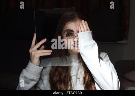 Adolescente tient une feuille transparent de perspex avec le dessin d'un demi-visage sur son propre visage pour montrer différentes émotions et sentiments Banque D'Images