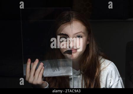 Adolescente tient une feuille transparent de perspex avec le dessin d'un demi-visage sur son propre visage pour montrer différentes émotions et sentiments Banque D'Images