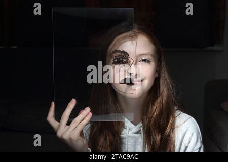 Adolescente tient une feuille transparent de perspex avec le dessin d'un demi-visage sur son propre visage pour montrer différentes émotions et sentiments Banque D'Images