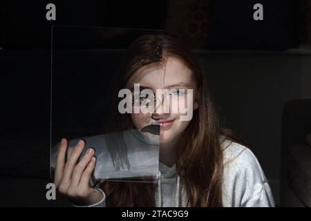 Adolescente tient une feuille transparent de perspex avec le dessin d'un demi-visage sur son propre visage pour montrer différentes émotions et sentiments Banque D'Images