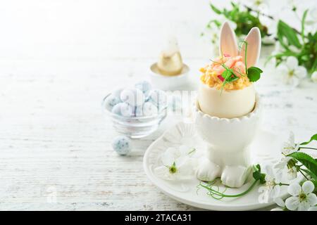 Œufs farcis ou vidés avec jaune, crevettes, micro-verts de pois avec paprika dans un support en forme de lapin pour la table de pâques décorer cerisier frais ou fleur de pommier Banque D'Images