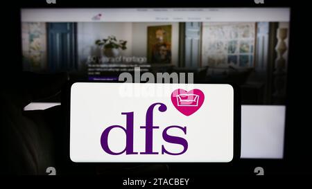 Personne détenant un smartphone avec le logo de la société de vente au détail britannique DFS Furniture plc devant le site Web. Concentrez-vous sur l'affichage du téléphone. Banque D'Images