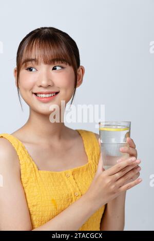 heureuse jeune femme asiatique souriante tenir un verre d'eau avec du citron Banque D'Images