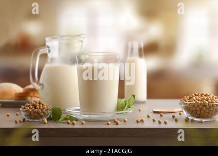 Récipients en verre avec du lait de soja et des grains dans des bols sur une table en bois dans une cuisine. Vue avant. Banque D'Images