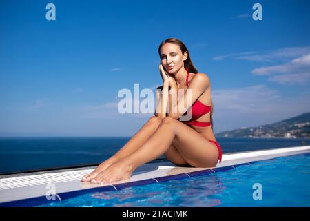 Jeune femme se détendant dans la piscine à débordement en regardant la vue. Heure d'été, plage, piscine, concept de vacances Banque D'Images