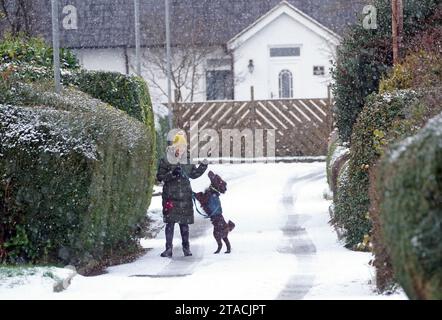 Une femme avec son chien dans la neige à Swarland, Northumberland. Les usagers de la route sont avertis de la présence de verglas alors que le met Office a émis des alertes de neige et de glace jaune pour de vastes régions d'Écosse, d'Angleterre et d'Irlande du Nord, alors que les températures chutent. Le service météorologique national a fait part de la probabilité que des personnes souffrent de glissades et de blessures par chute dans l'une des premières périodes glaciales de l'hiver. Date de la photo : jeudi 30 novembre 2023. Banque D'Images