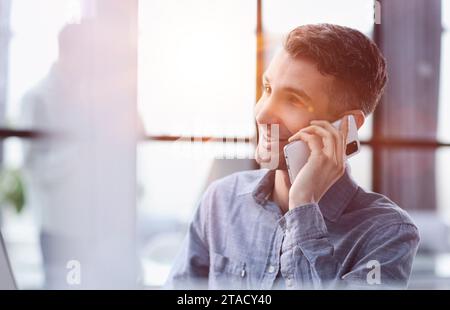 Bien sûr, nous pouvons le faire pour vous. Un jeune homme d'affaires parlant au téléphone tout en étant assis à son bureau. Banque D'Images