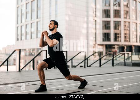 Faites avancer l'homme qui fait une fente. Le sport dans le concept de la grande ville. Homme fort qui étire les jambes avant de faire du jogging. Concept de soins de santé. Coureur de sport noir. Urb Banque D'Images