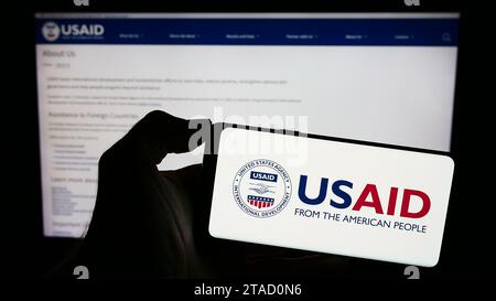 Personne tenant un téléphone portable avec le logo de l'Agence des États-Unis pour le développement international (USAID) devant la page Web. Concentrez-vous sur l'affichage du téléphone. Banque D'Images