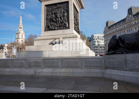 Deux jeunes femmes assises sur les marches au pied de la colonne Nelson, Trafalgar Square, Londres Banque D'Images