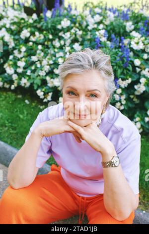 Portrait de mode en plein air de femme élégante de 50 - 55 ans, portant la tenue colorée, posant au parc de fleurs d'été Banque D'Images