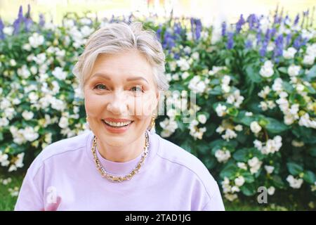 Portrait de mode en plein air de femme élégante de 50 - 55 ans, portant la tenue colorée, posant au parc de fleurs d'été Banque D'Images