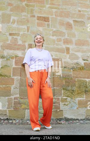 Portrait de mode en plein air de femme mature élégante avec les cheveux gris, portant un haut violet et un pantalon orange Banque D'Images