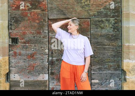 Portrait de mode en plein air de femme mature élégante avec les cheveux gris, portant un haut violet et un pantalon orange Banque D'Images