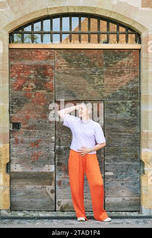 Portrait de mode en plein air de femme mature élégante avec les cheveux gris, portant un haut violet et un pantalon orange Banque D'Images