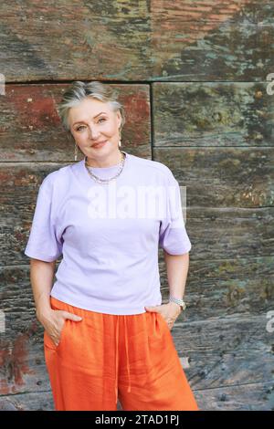 Portrait de mode en plein air de femme mature élégante avec les cheveux gris, portant un haut violet et un pantalon orange Banque D'Images