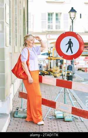 Portrait de mode en plein air de femme mature élégante avec les cheveux gris, portant un haut violet et un pantalon orange Banque D'Images